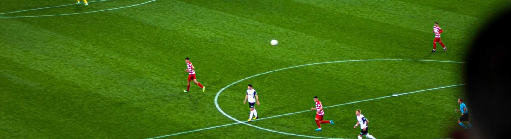 Jugadores durante un partido de fútbol, con el balón en el aire cerca del círculo central
